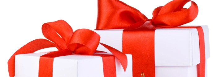 Close‑up of two white gift boxes wrapped with wide, shiny red ribbons