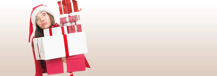 Person wearing a red outfit carrying a tall stack of wrapped gift boxes in various sizes