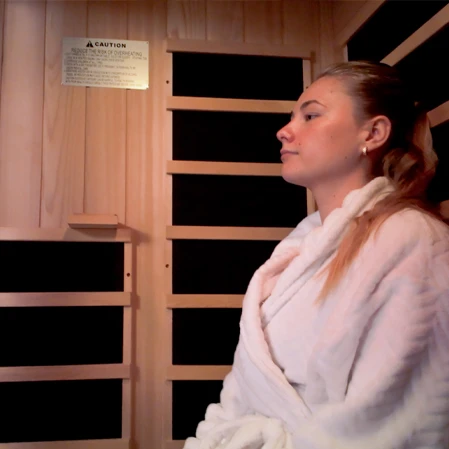 A person wearing a white plush robe sits inside a wooden infrared sauna