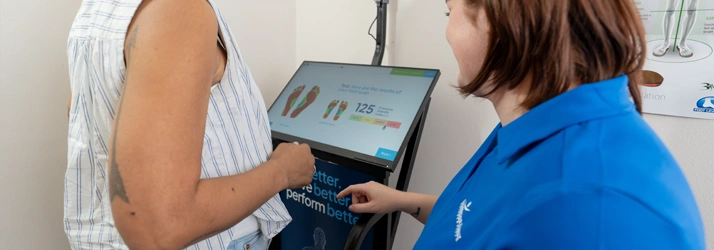 A person in a sleeveless striped top stands at an electronic foot‑scanning device