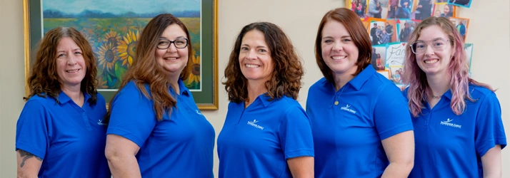 A group of five individuals wearing matching blue collared shirts stands indoors