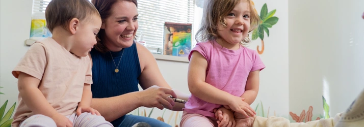 An individual sits on a cushioned surface with two young children beside them