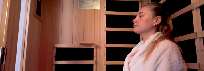 A person wearing a light-colored robe sits inside a wooden infrared sauna