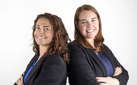 Two individuals wearing black coats in front of white background